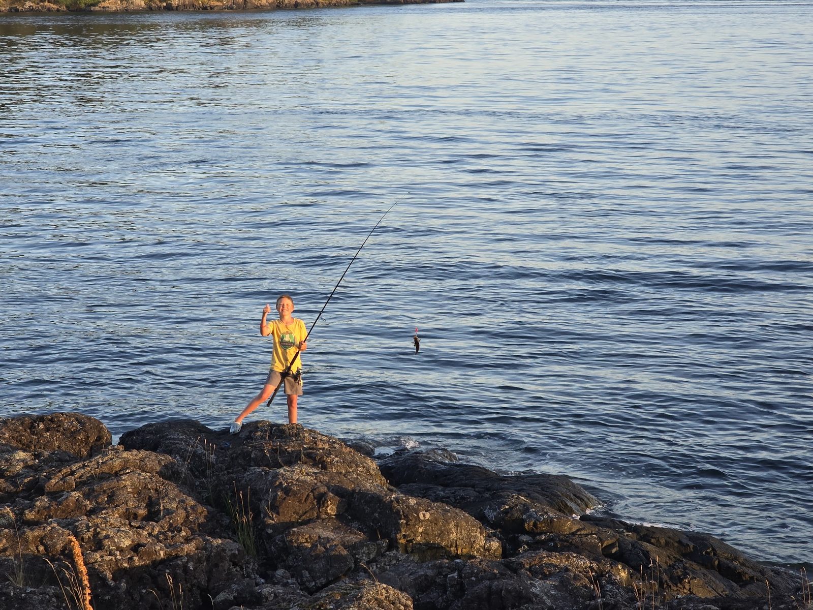 A kid shore-fishing from the rocks at golden hour